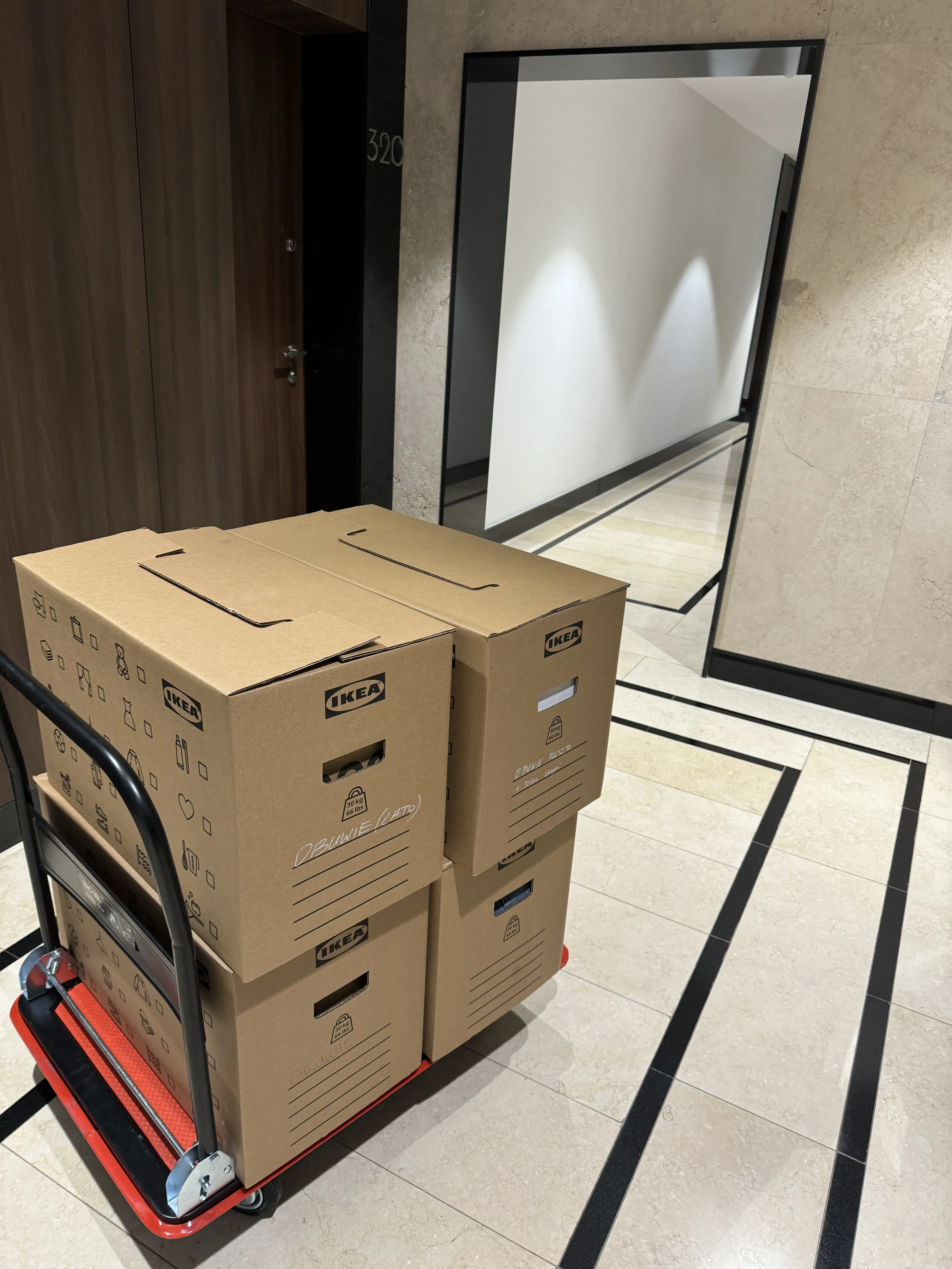 Czerwony wózek transportowy załadowany kartonami IKEA z napisami Obuwie na klatce schodowej